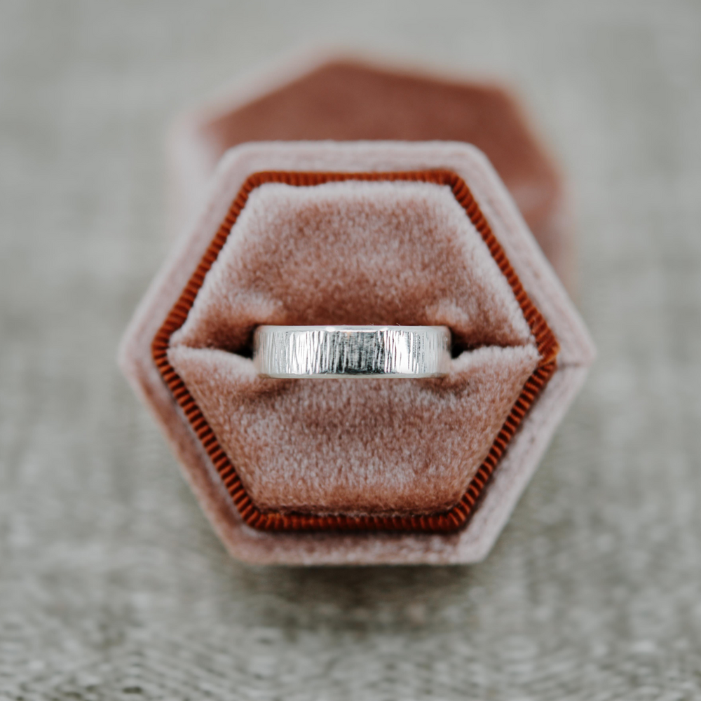 Ethical wedding ring. Bevelled hammered ring in white gold sits in a pink velvet ring box. 